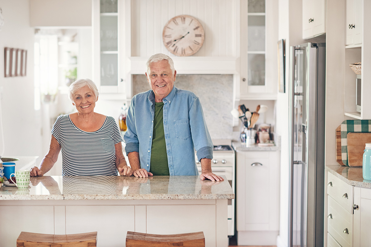 Portrait of a content senior couple smiling while standing happily together in their kitchen at home