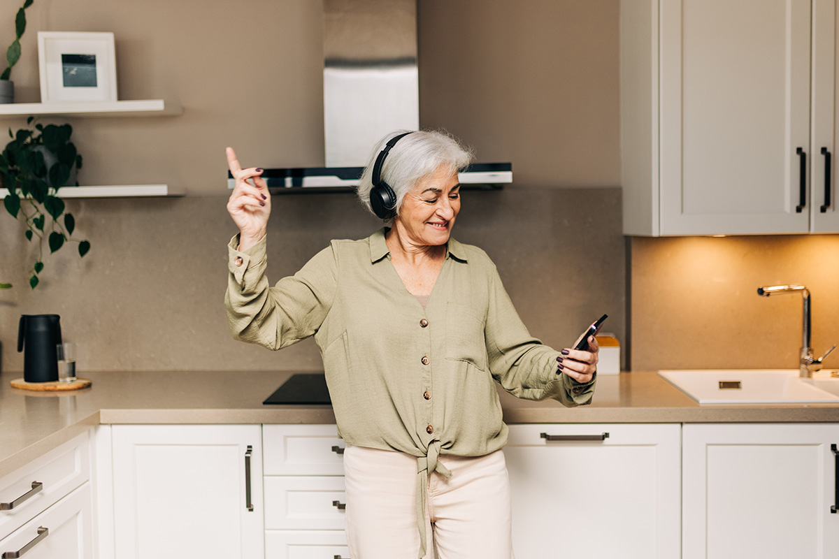 Smiling elderly woman dancing to her favorite music while wearing wireless headphones.
